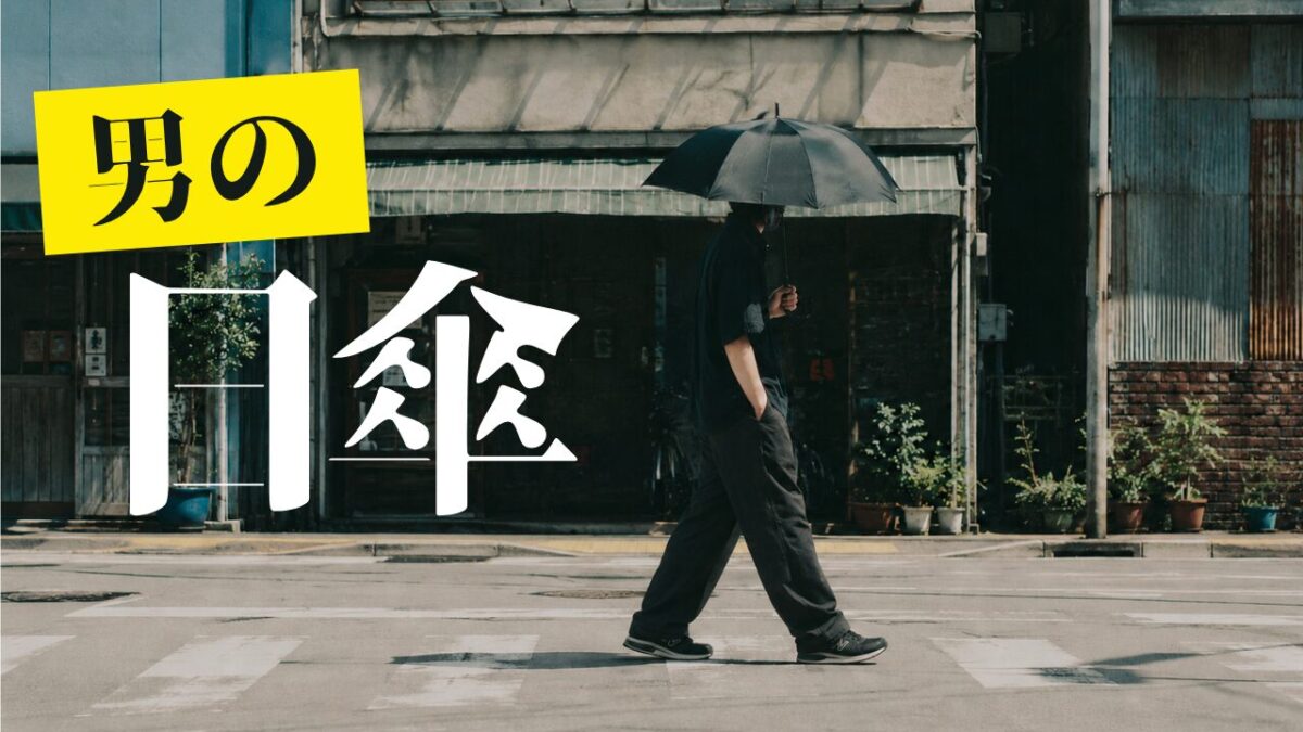 黒い日傘を差して街中を歩く30代男性のファッションイメージ
