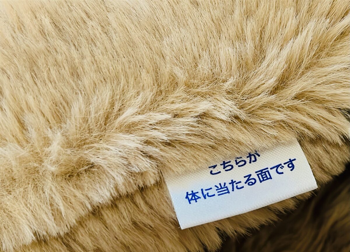 毛足の長い生地に縫いつけられた「こちらが体に当たる面です」と書かれた白いタグ